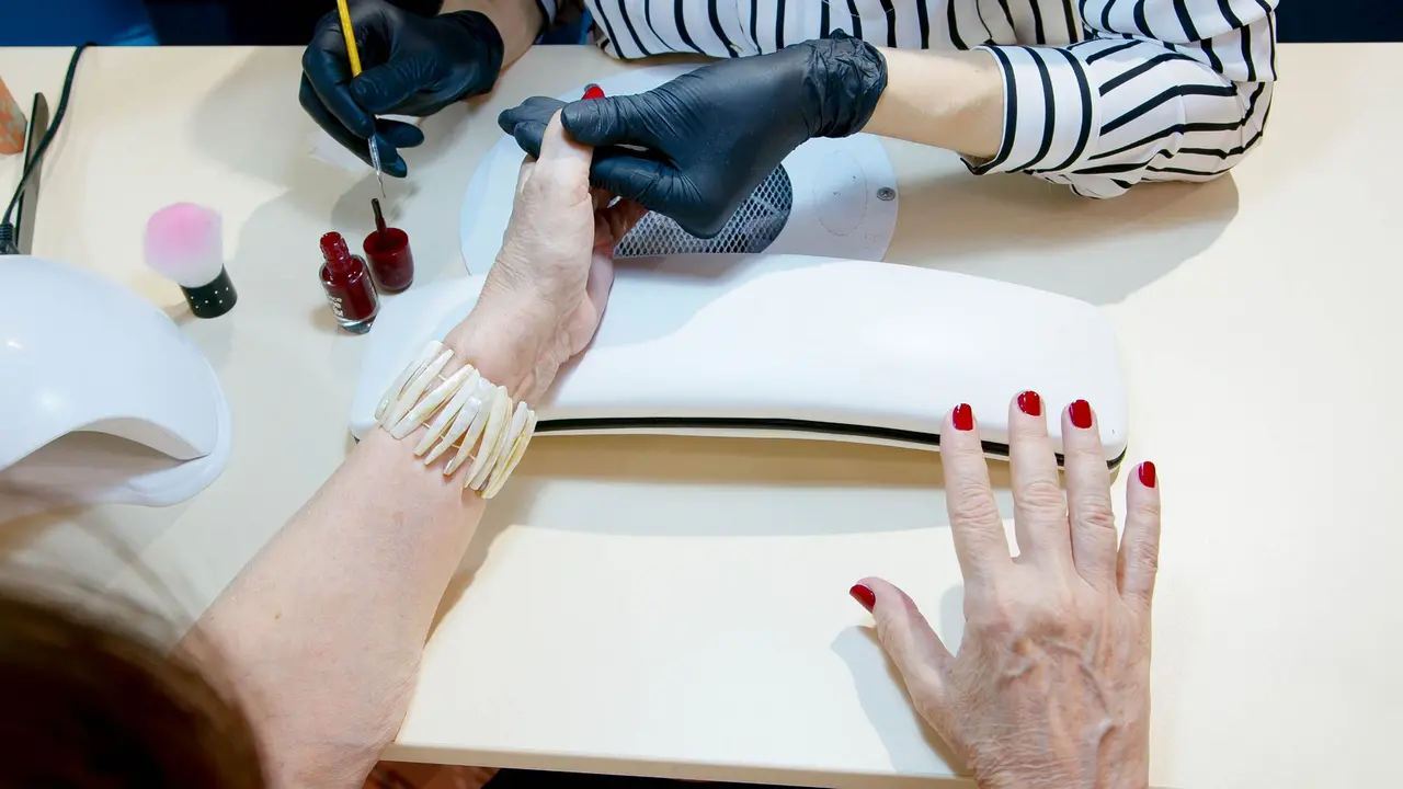 Eine Nageldesignerin lackiert die Nägel einer Kundin